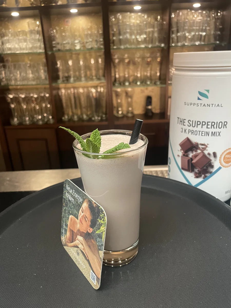 Frisch zubereiteter Proteinshake mit Minze und Bierdeckel vor einem Regal mit Gläsern in der Gastronomie des Neptunbad